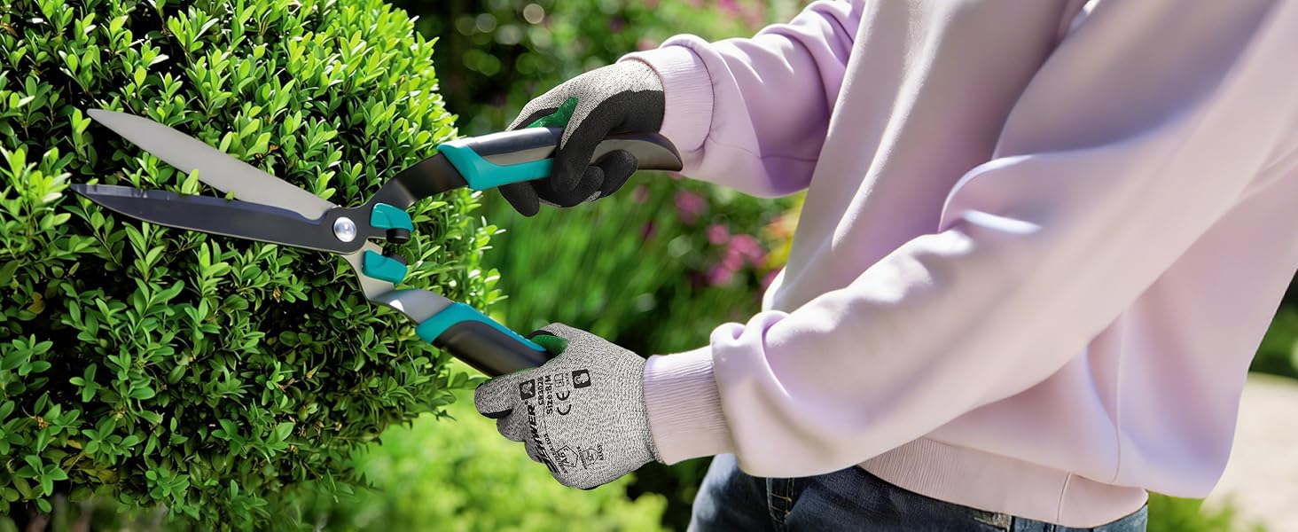 Person trimming a bush with garden shears in a garden setting