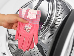 Hand wearing a pink glove holding a cleaning product in front of a washing machine.