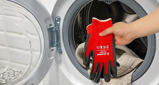 Person wearing red gloves with cleaning symbols holding a cloth in front of an open washing machine.