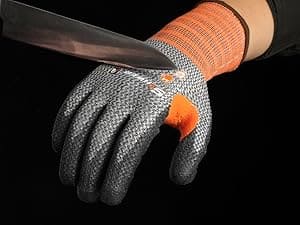 Hand wearing a gray and orange glove holding a knife against a black background