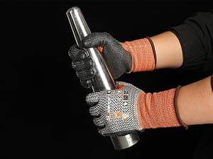 Person wearing cut-resistant gloves holding a metal object against a black background