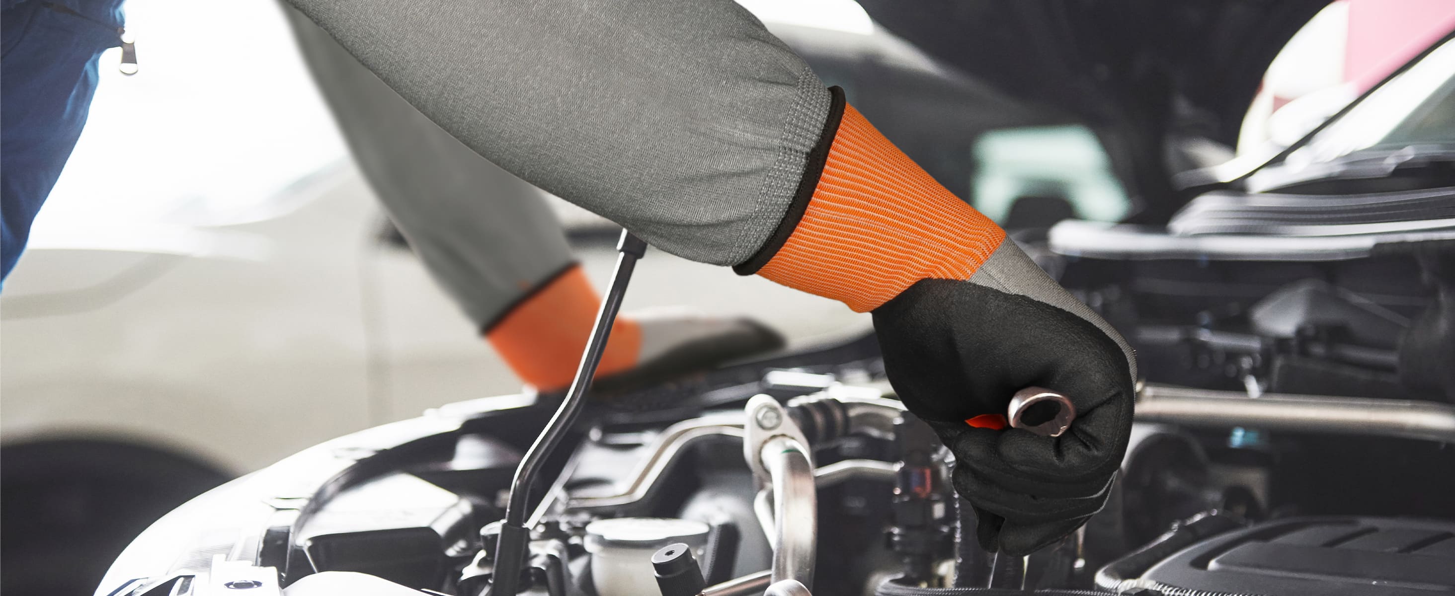 Person checking car engine with a dipstick, wearing orange gloves.