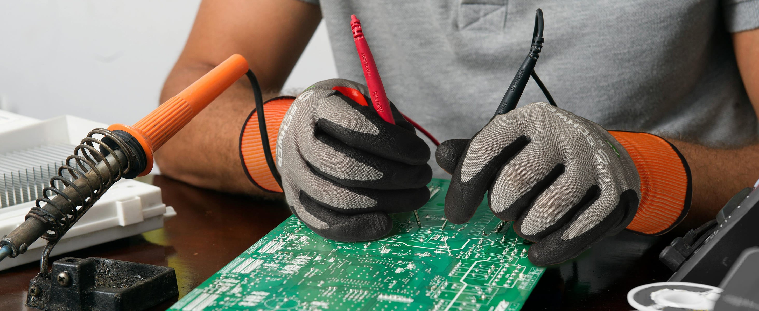 Person wearing gloves working on a circuit board with tools on a table.