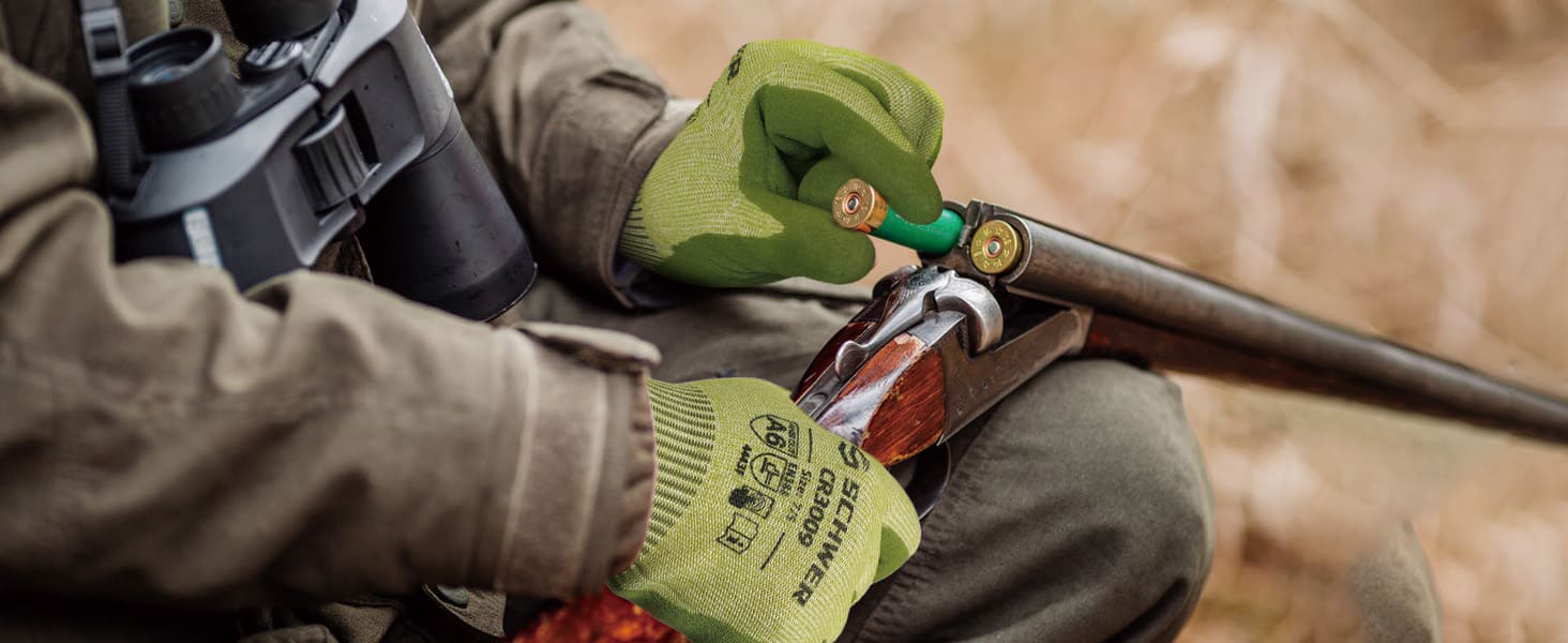 Person in hunting gear with binoculars and a rifle, wearing green gloves.