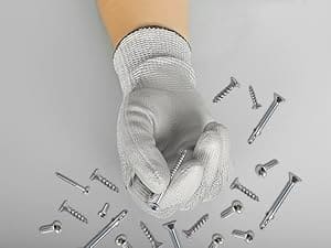 Hand wearing a glove holding a screw with screws scattered on a gray background