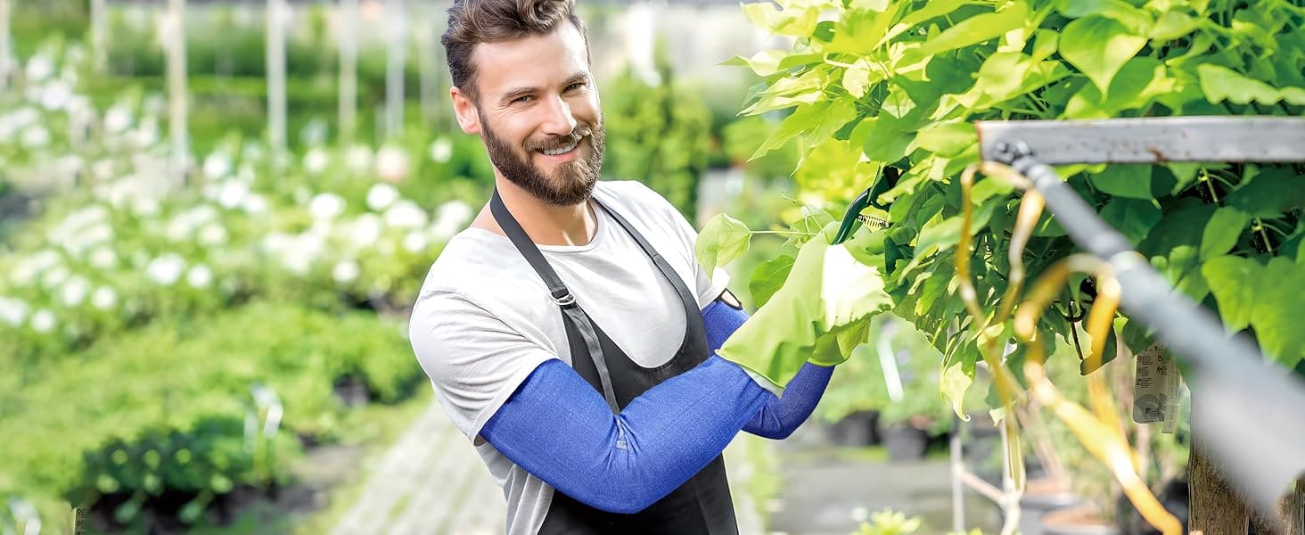 Man in a garden wearing an apron and blue sleeves, standing among plants.