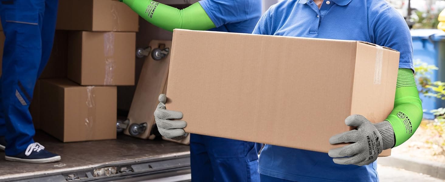 Two movers in blue uniforms and green gloves carrying a cardboard box from a van.
