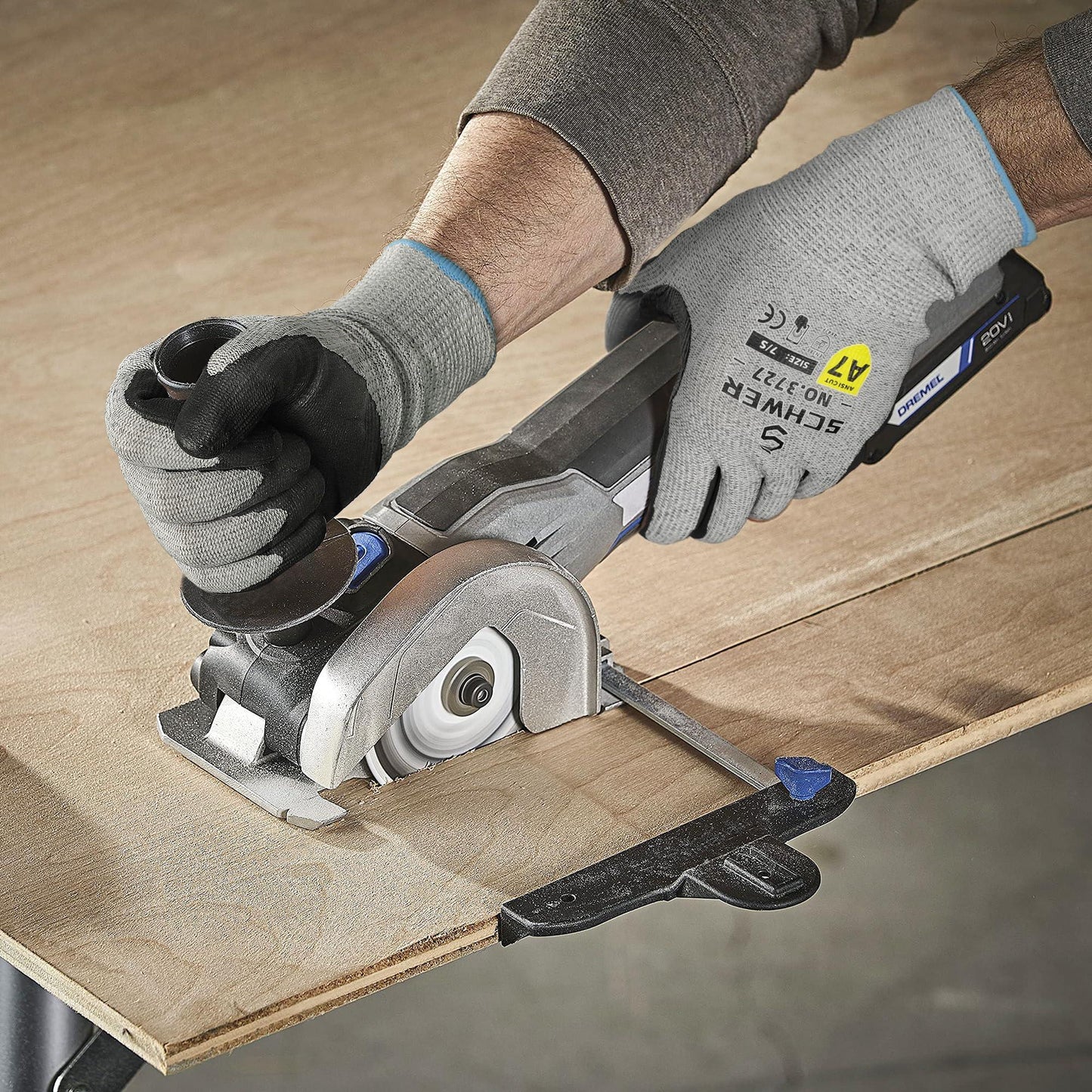 person wearing grey gloves using a cordless Dremel circular saw to cut plywood on a workbench