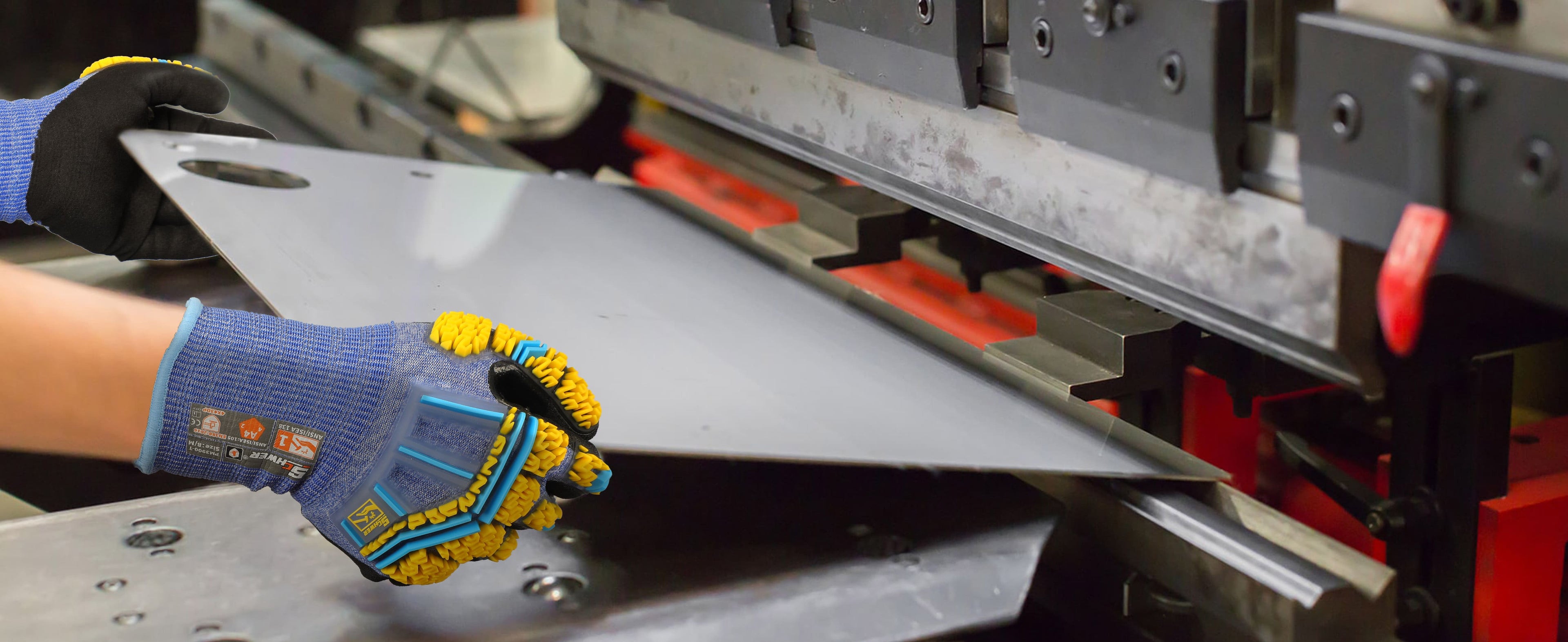Person wearing gloves holding a metal sheet in front of a metal cutting machine.