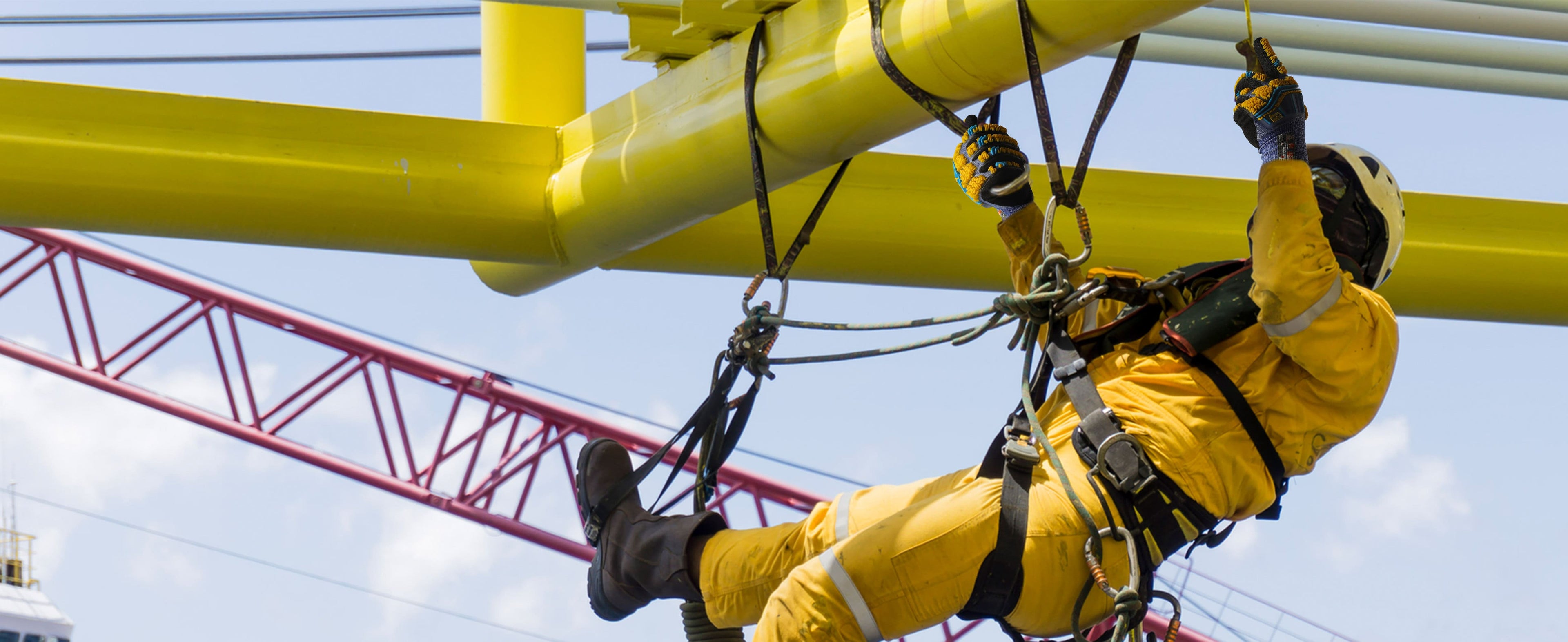 Person in yellow safety gear working on a large yellow structure with a crane in the background.