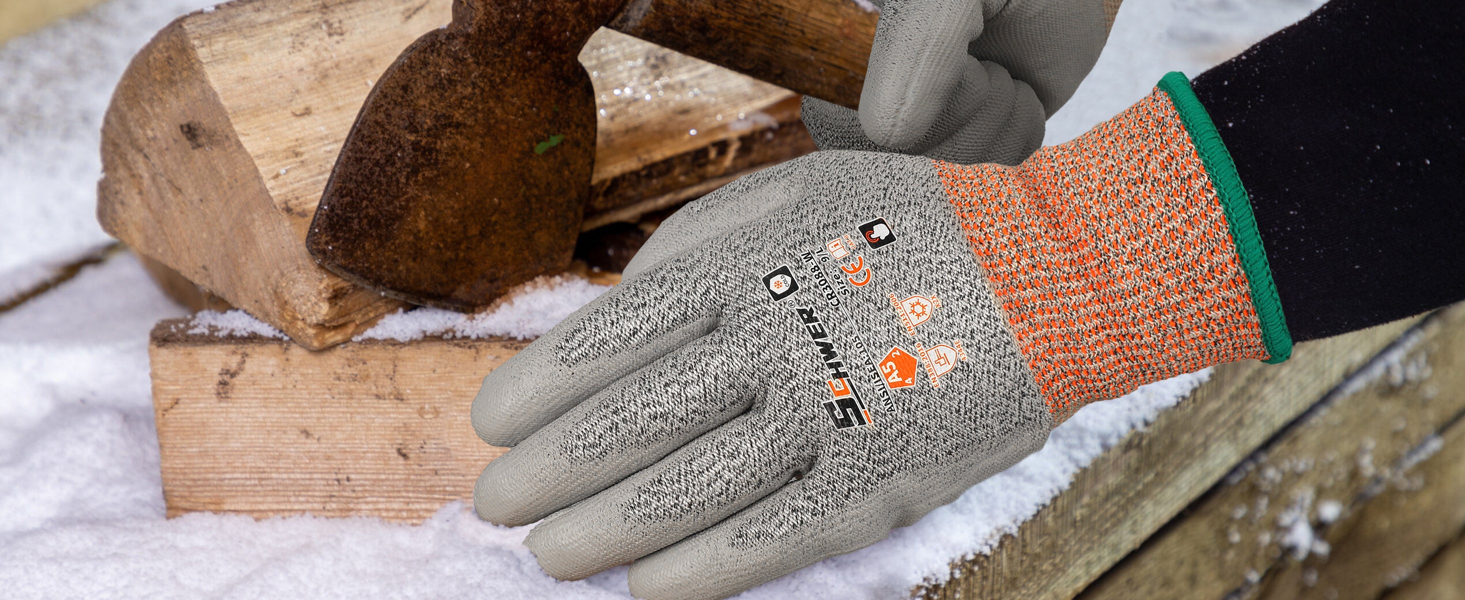 Hand wearing a cut-resistant glove with a background of stacked firewood and snow.