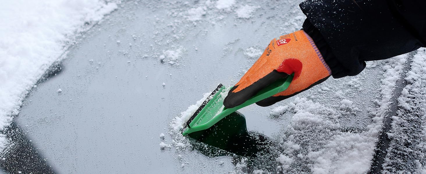 Person using a green and orange ice scraper on a car window with snow and ice.