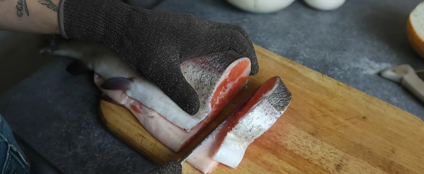 Person cutting fish on a wooden board with a knife, wearing a black glove.