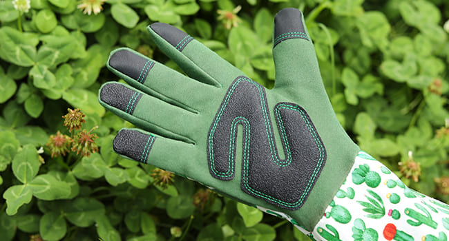 Green gardening glove with black accents on a green leafy background
