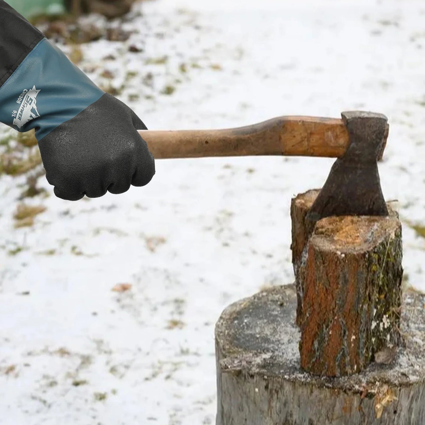Gloved hand holding axe splitting wood log on snowy surface outdoors