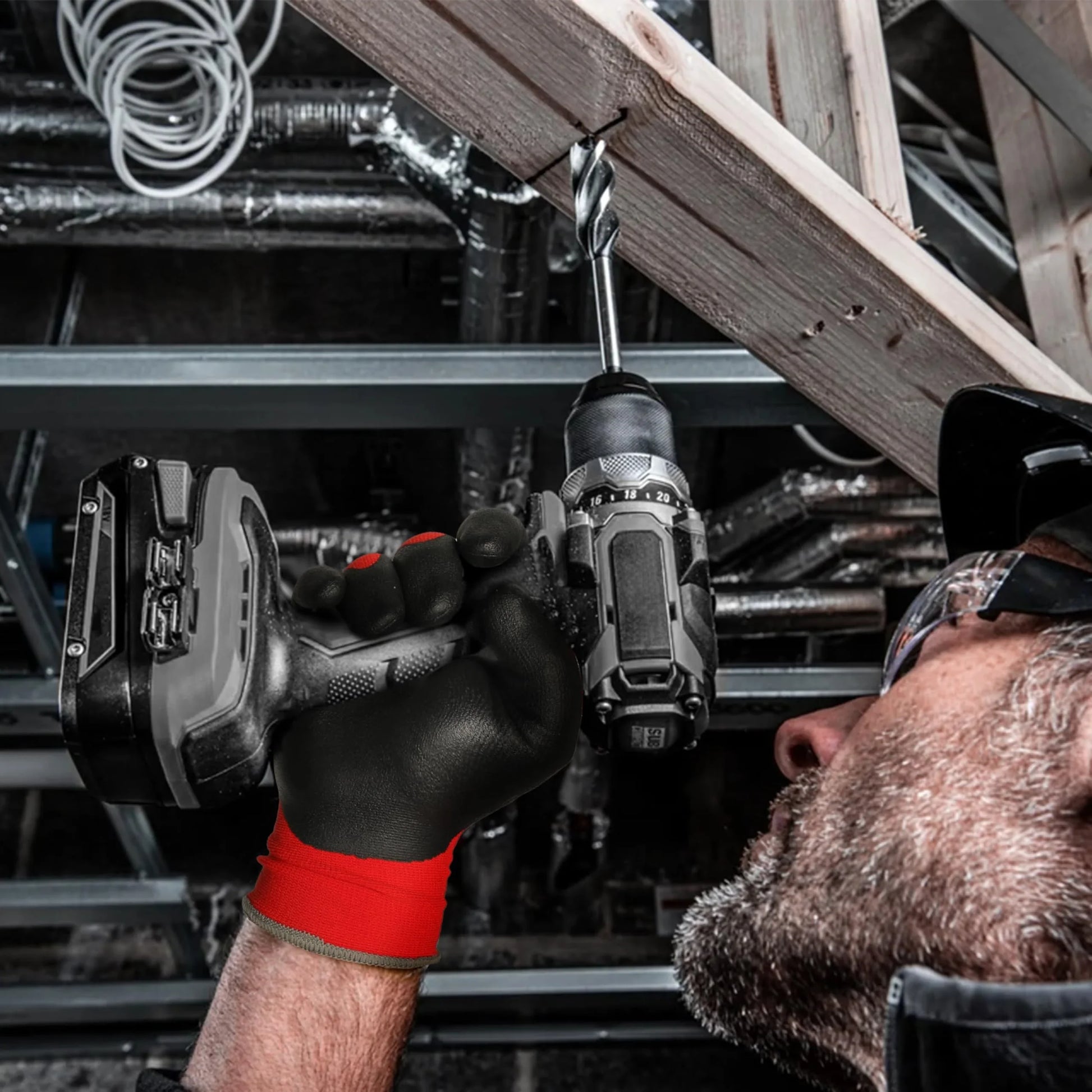 Man wearing Schwergloves black and red work gloves using a cordless drill on a wooden beam in construction setting