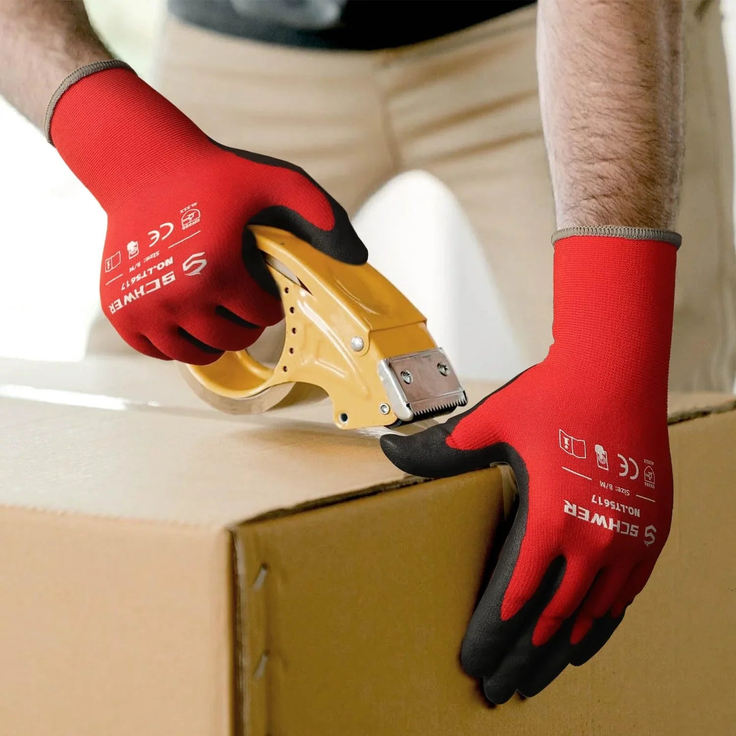 Hands wearing red and black Schwergloves cutting tape on cardboard box with tape dispenser