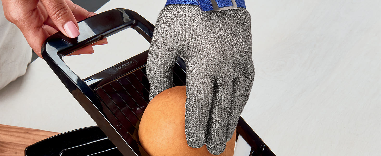 Person wearing a metal mesh glove holding a smartphone above a cutting board with a knife.