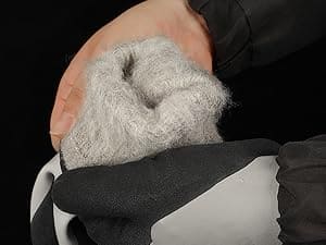 Hand wearing a black glove holding a gray textured object against a dark background