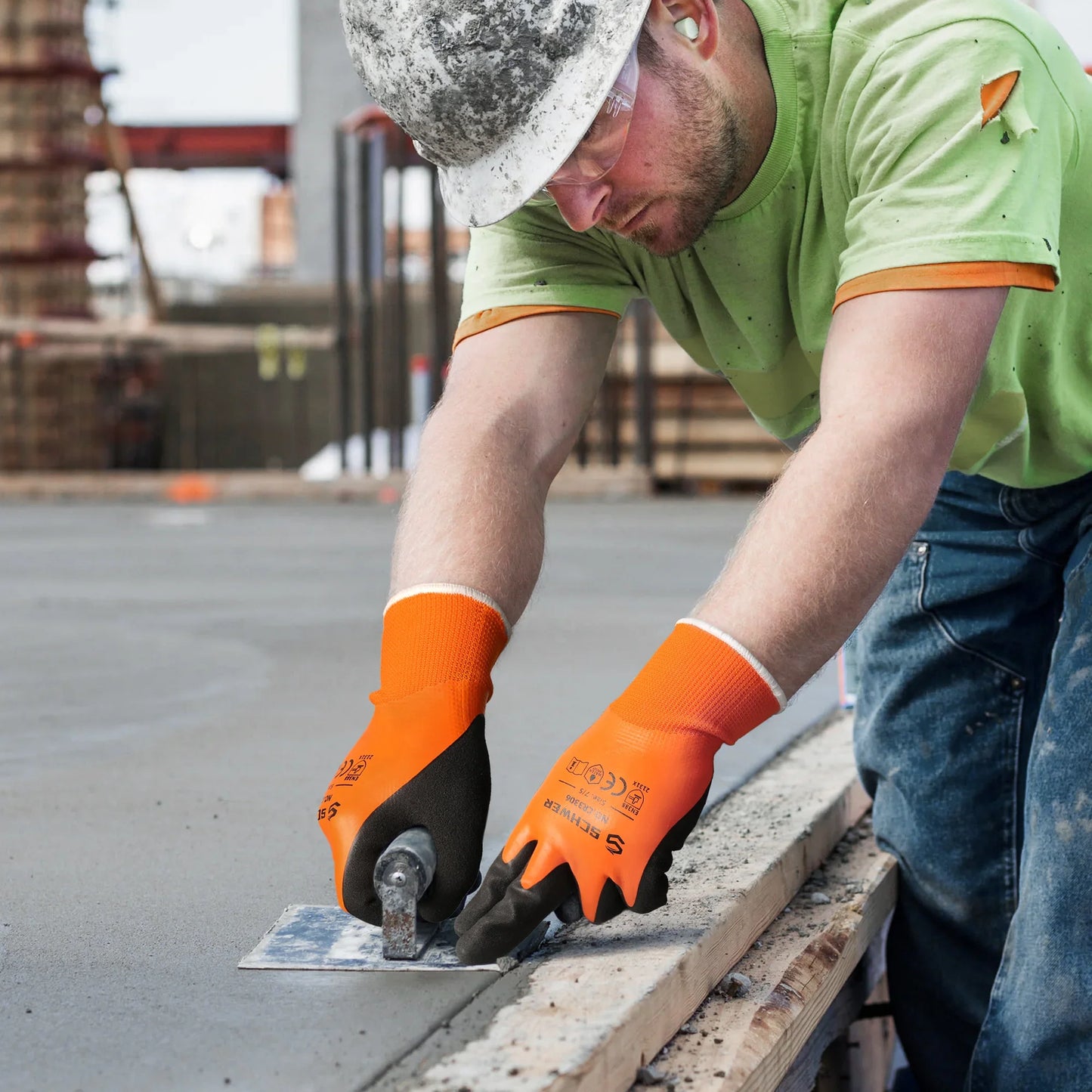 Construction worker wearing orange gloves and a hard hat smoothing freshly poured concrete on a building site